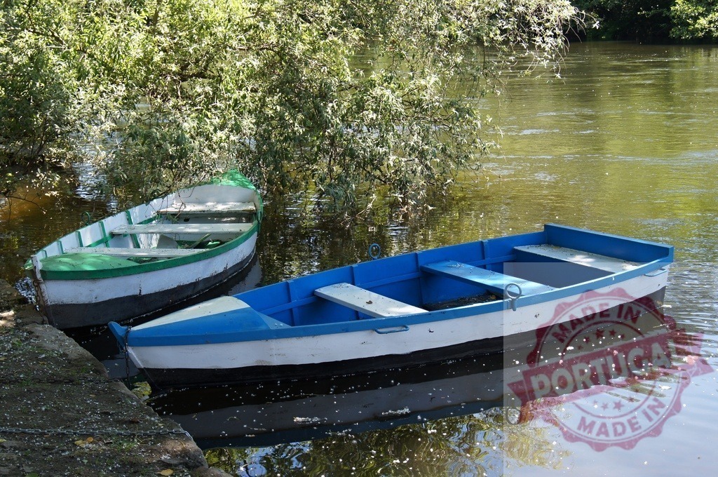Two colorful wooden rowboats mooring on calm river water | Wooden rowboats resting on calm river with green trees reflecting in water - Realized with Pictrs.com