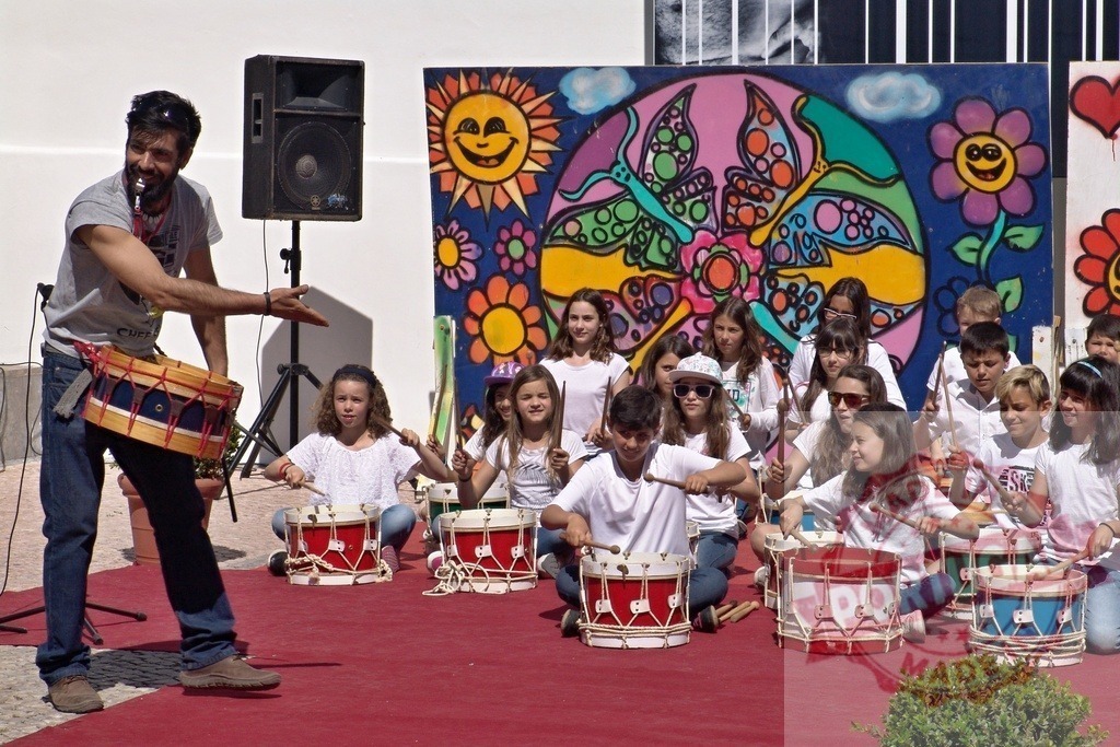 Music teacher leading children drumming lesson outdoors | Music teacher leading a group of children playing drums during an outdoor music class - Realisiert mit Pictrs.com