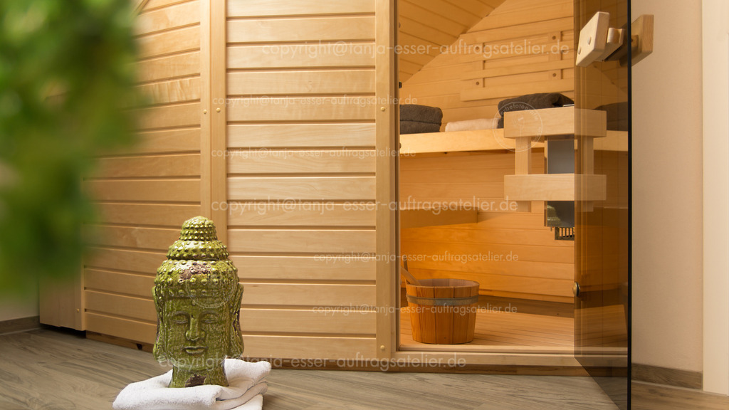 Wellness im Alltag durch eine integrierte Sauna in einem Badezimmer.  | Eine kleine Sauna mit 2 Holzliegestühlen. Kleine Kabine in einem Badezimmer. Im Vordergrund steht ein kleiner Buddha.