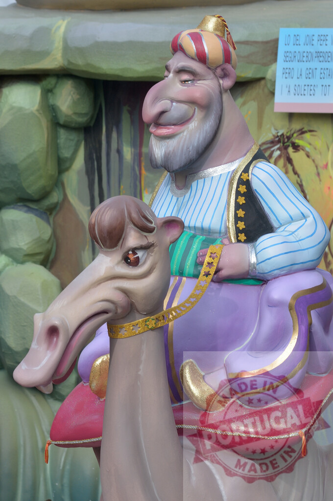 Fallas festival character riding a camel street art | Exaggerated caricature sculpture depicting a man riding a camel, part of the Fallas festival - Realized with Pictrs.com