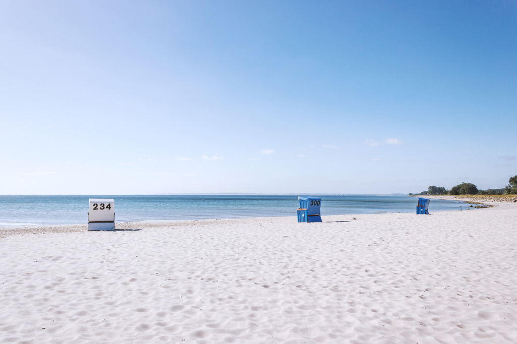 Wandbild: Strandkörbe in Damp – Küstenruhe an der Ostsee | Dieses maritime Wandbild aus Damp zeigt eine Reihe nummerierter Strandkörbe, die ruhig auf dem hellen Sandstrand stehen und den Blick auf die weite Ostsee freigeben. Die klare Küstenlinie, das sanfte Wasser und die offene Himmelsstimmung verleihen dem Motiv eine entspannte, nordische Atmosphäre. Die Aufnahme fängt die typische Strandszenerie von Damp ein, in der Strandkörbe, Meer und Weite eine harmonische, maritime Gelassenheit erzeugen.