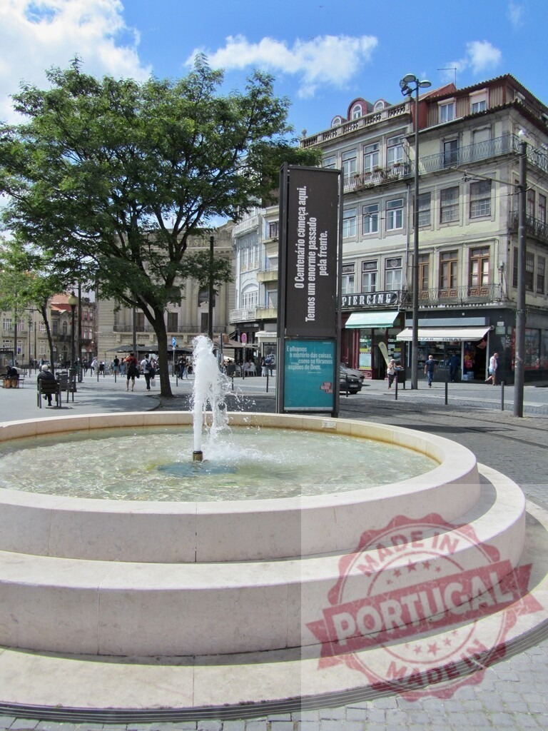 Porto city square with an active water fountain | Stone water fountain flowing in a city square, surrounded by buildings and a large green tree - Realized with Pictrs.com