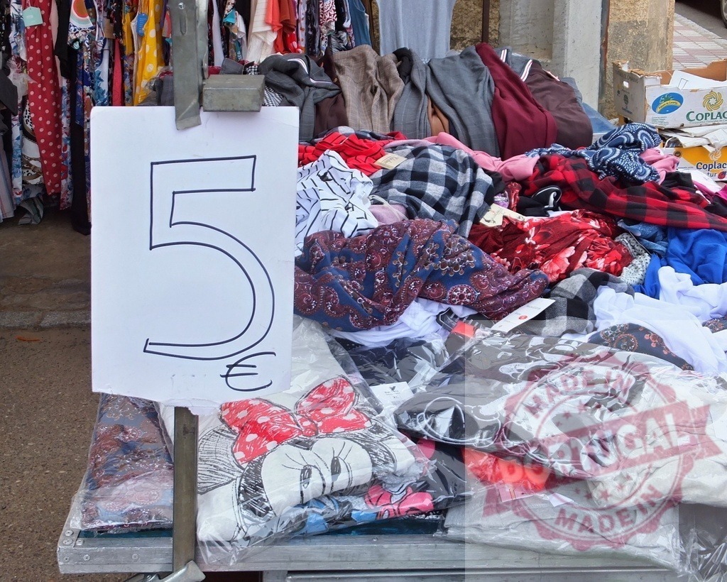 Street market clothing stall offering 5 euro sale | Clothing items piled high on a street market stall with a prominent 5 euro price sign - Realisiert mit Pictrs.com