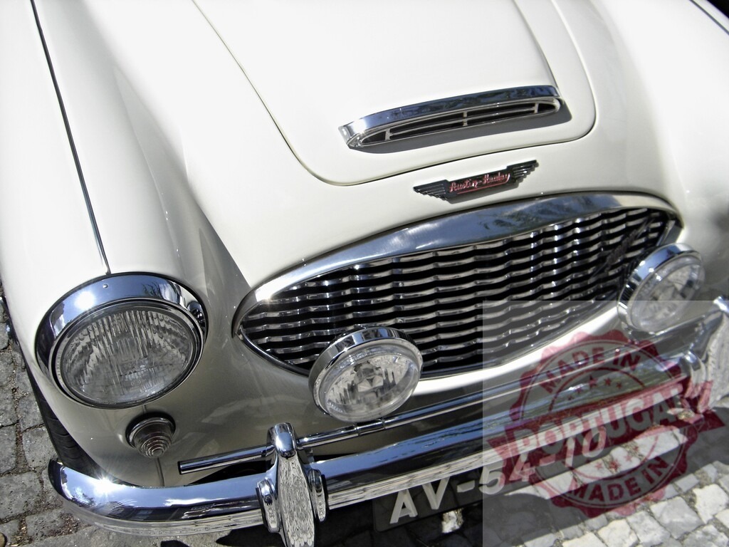 White Austin-Healey Sprite grille and headlights shining in the sun | Close-up of a white Austin-Healey Sprite's front, featuring the iconic grille, headlights, and hood ornament - Realisiert mit Pictrs.com
