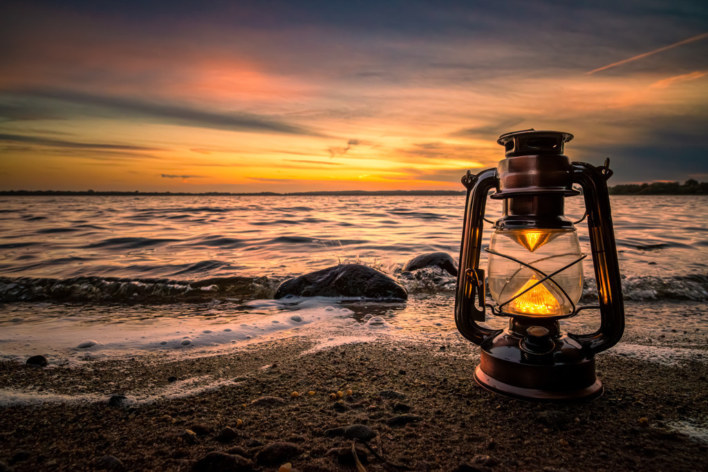 Abendstunde am Wittensee | Auf diesem atemberaubenden Foto, das an der Badestelle des Wittensees aufgenommen wurde, sehen wir eine Szene von unvergleichlicher Schönheit. Im Vordergrund steht eine leuchtende Öllampe, deren warmes, flackerndes Licht die Umgebung in ein Glühen taucht. 
Der eigentliche Höhepunkt dieses Bildes ist jedoch der traumhafte Sonnenuntergang, der sich am Horizont entfaltet. Die Sonne ist bereits am Horizont verschwunden und taucht den Himmel in ein buntes Farbenmeer.
Dieses Bild ist ein wahrer Augenschmaus und lädt dazu ein, in die Ruhe und Magie dieses besonderen Ortes einzutauchen.
