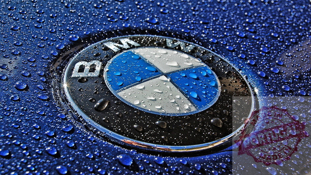 Close-up of BMW logo with water droplets on blue car surface | Shiny BMW logo is covered in water droplets on a blue car surface, creating a luxurious and clean aesthetic - Realisiert mit Pictrs.com