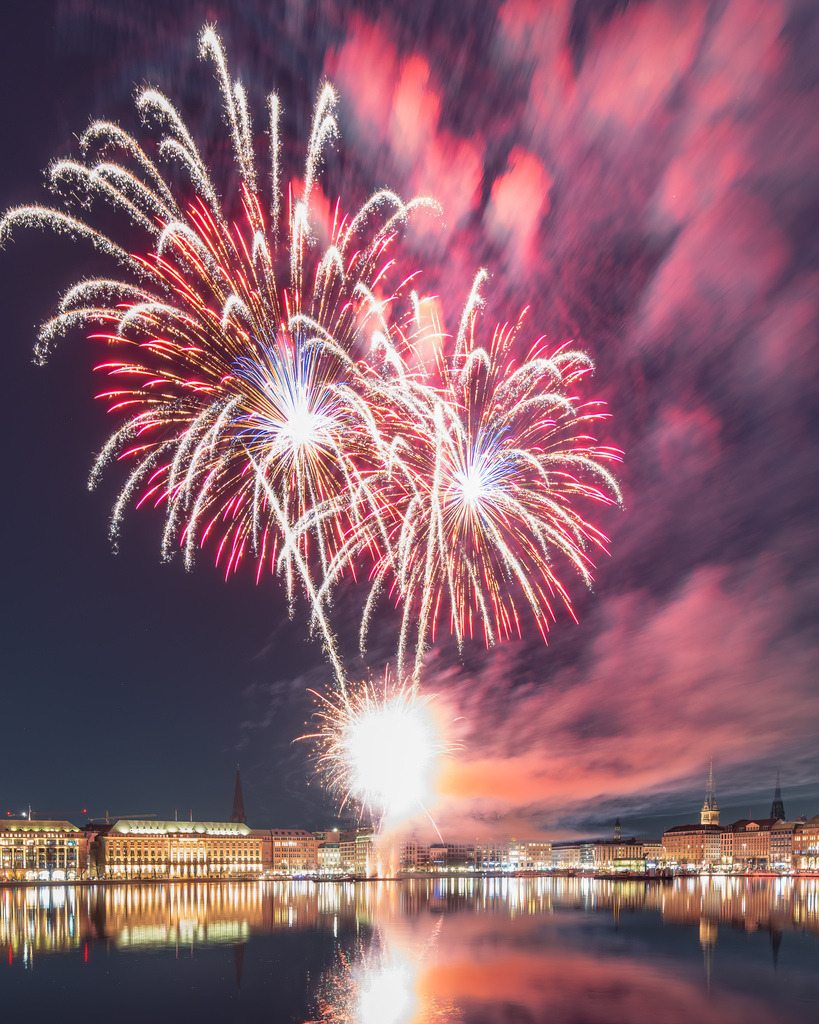 Feuerwerksfinale über der Alster | Ein dichtes Meer aus weißen, roten und goldenen Feuerwerksbahnen füllt den Himmel über Hamburg. Die dramatischen Wolken verstärken die intensive Wirkung der Aufnahme. - Realisiert mit Pictrs.com