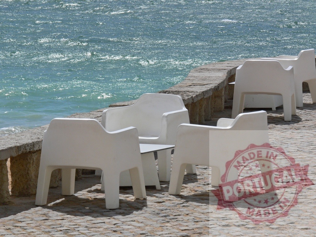 Empty white plastic chairs reflecting on waterfront promenade | White plastic chairs and small tables standing empty on a stone promenade by the ocean - Realized with Pictrs.com