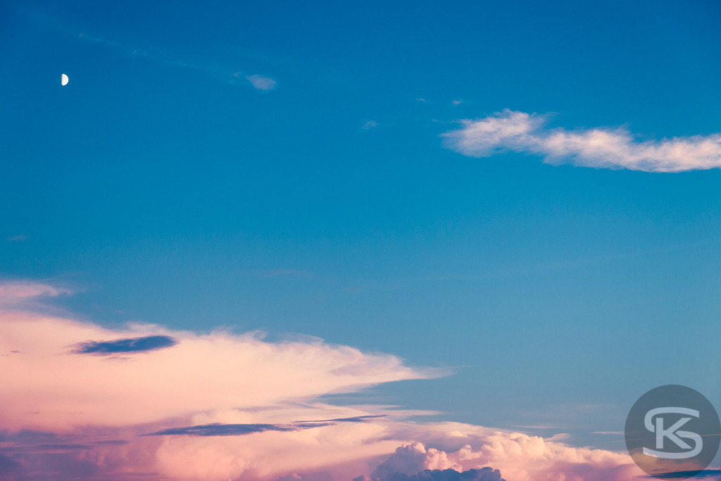 Pastellfarbener Himmel bei Sonnenaufgang / Sonnenuntergang mit Mondsichel | Ein ruhiges und friedliches Bild des Himmels während der Dämmerung. Zarte rosa und weiße Wolken ziehen über das leuchtend blaue Firmament, während eine kleine Mondsichel still am oberen Rand sichtbar ist. Die ästhetische und stimmungsvolle Atmosphäre lädt zum Träumen und Entspannen ein. - Realisiert mit Pictrs.com
