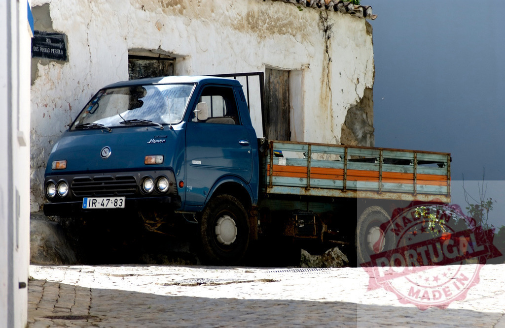 Blue vintage flatbed truck parked in Portuguese village | Blue vintage flatbed truck parked on cobblestone street in a historic Portuguese village - Realized with Pictrs.com
