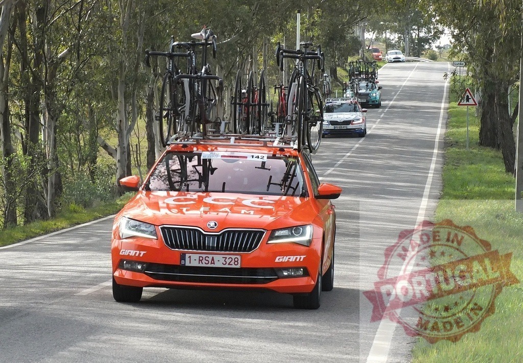 Team car carrying bicycles on a race road | Orange CCC team car driving on a tree-lined road with bikes on the roof rack - Realized with Pictrs.com