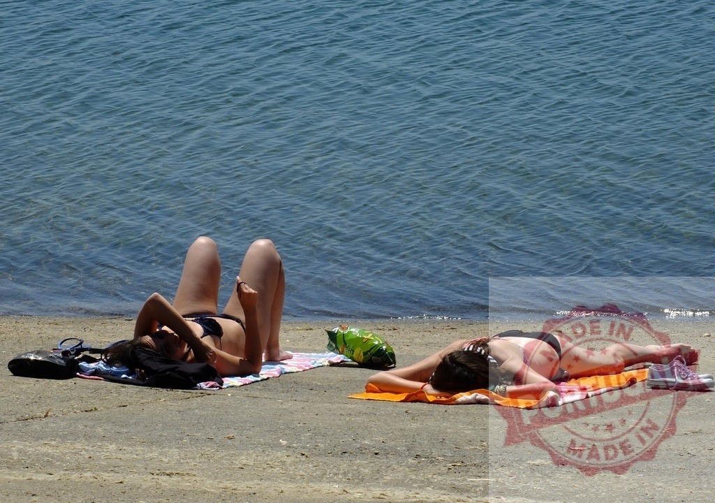 Women sunbathing and relaxing on beach by ocean. Spain - Extremadura | Two women relaxing on towels, sunbathing on a sandy shore by the water - Realized with Pictrs.com