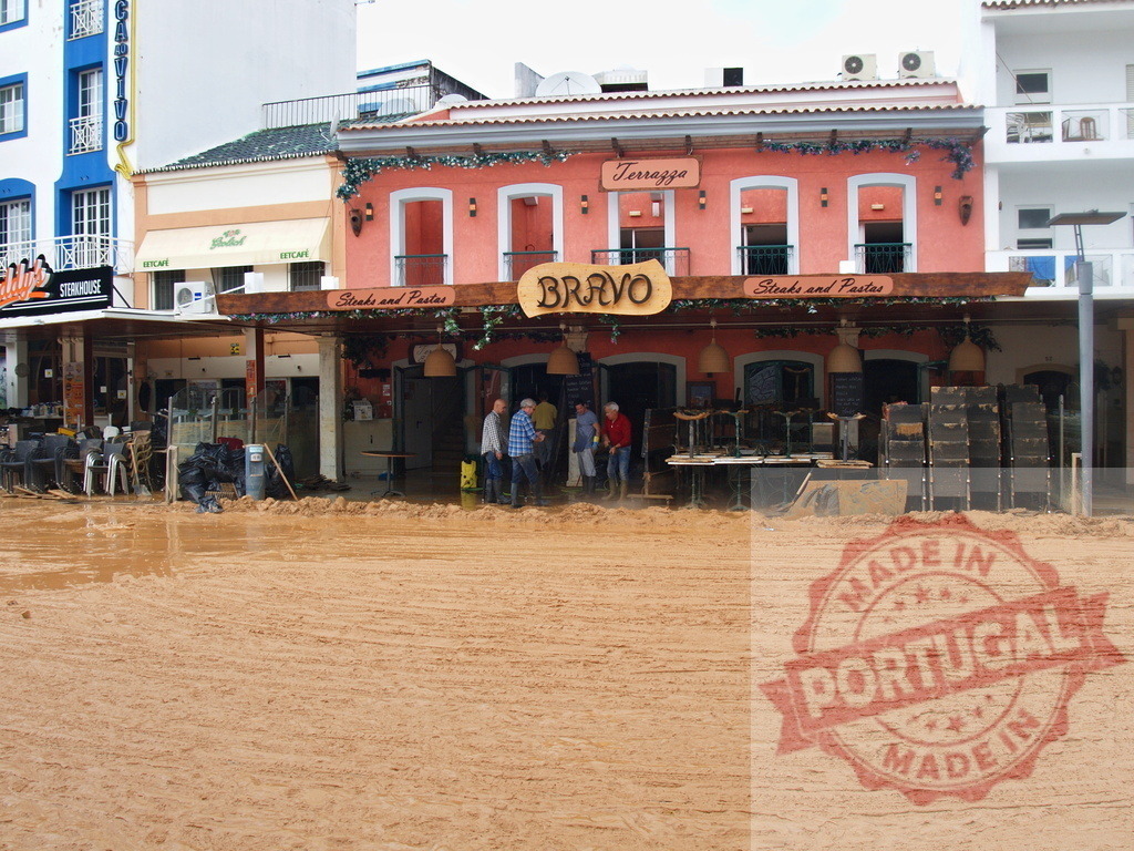 Flood aftermath street showing thick mud and restaurant cleanup | Albufeira Flood - discruction by weather problems People cleaning mud from a restaurant after a natural disaster flood - Realisiert mit Pictrs.com