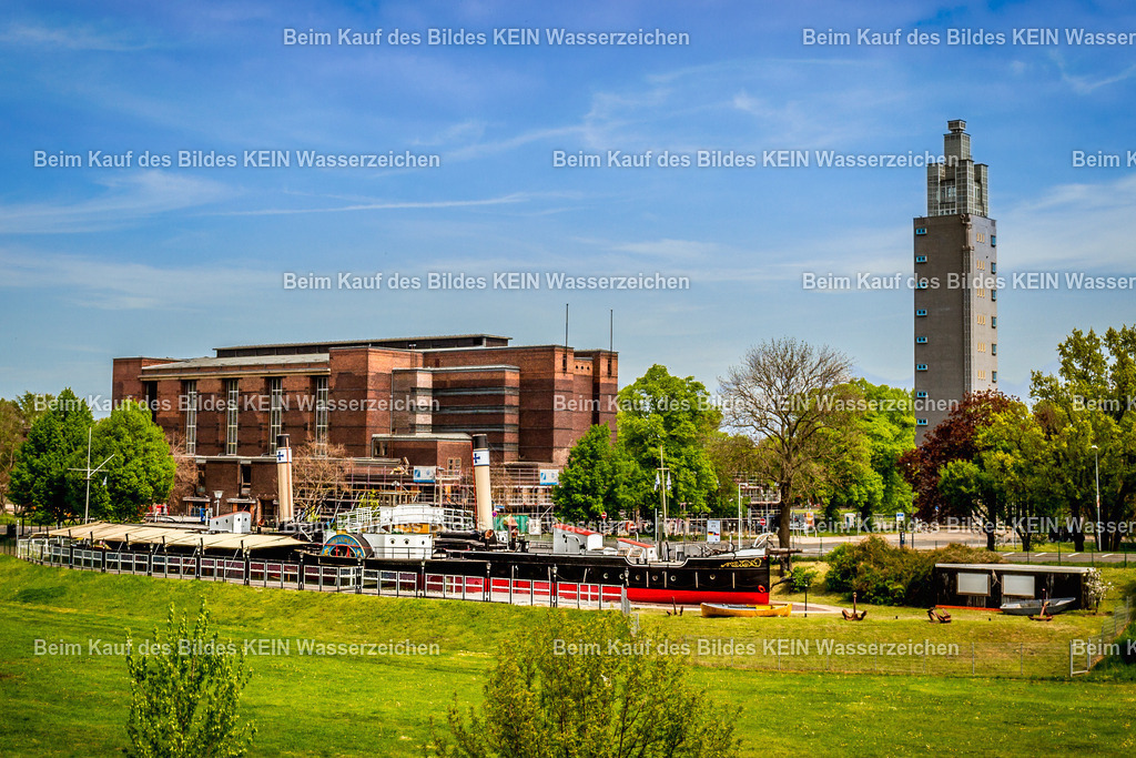 Magdeburg Sehenswürdigkeiten Schiffsmuseum Württemberg und Stadthalle mit Aussichtsturm albin Müller-9432 | Das Luftbild zeigt den historischen Elbeseitenradschleppdampfer „Württemberg“ im Magdeburger Rotehornpark aus einer Drohnenperspektive. Das Museumsschiff liegt dauerhaft auf seinem Ausstellungsgelände und beeindruckt mit seinen beiden markanten Schaufelrädern, dem hohen Schornstein und der charakteristischen Silhouette eines Dampfschleppers des frühen 20. Jahrhunderts. Aus der Vogelperspektive werden die technische Konstruktion und die Dimensionen des Schiffes besonders deutlich sichtbar.Die „Württemberg“ wurde 1908/1909 auf der Schiffswerft Gebrüder Sachsenberg in Roßlau gebaut. Der Raddampfschlepper ist 63,8 Meter lang und 15,7 Meter breit über die Radkästen. Angetrieben wurde das Schiff von einer Zweizylinder-Verbunddampfmaschine mit rund 625 PS, die zwei Seitenräder mit einem Durchmesser von 3,52 Metern bewegte. Mit nur 0,83 Metern Tiefgang war die „Württemberg“ speziell für die flachen Wasserstände der Elbe ausgelegt und konnte schwere Schleppverbände flussaufwärts transportieren. Seit 1974 ist sie als Museumsschiff in Magdeburg erhalten. ([Wikipedia][1])Die Drohnenaufnahme dokumentiert eindrucksvoll eines der bedeutendsten technischen Denkmäler der deutschen Binnenschifffahrt. Die „Württemberg“ zählt zu den letzten erhaltenen Elbeseitenradschleppern und erinnert an eine Epoche, in der dampfbetriebene Schleppschiffe den Güterverkehr auf der Elbe über Jahrzehnte prägten. - Realisiert mit Pictrs.com