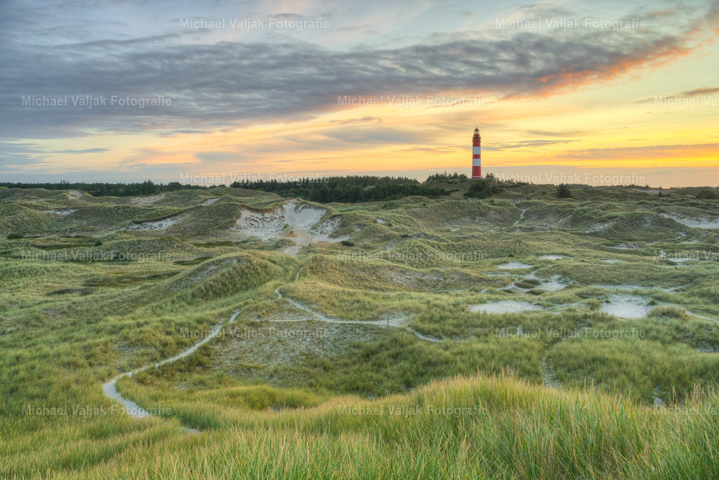 Leuchtturm auf Amrum bei Sonnenaufgang | Der Amrumer Leuchtturm, ein Wahrzeichen der Nordseeinsel Amrum in Deutschland, ist besonders bei Sonnenaufgang ein atemberaubender Anblick. Wenn die ersten Strahlen des Tages den Himmel erleuchten, zeichnet sich die Silhouette des Leuchtturms scharf gegen die erwachende Dämmerung ab. Dieses Schauspiel der Natur, verstärkt durch das historische Bauwerk, bietet ein perfektes Motiv für Fotografen und ist ein magischer Moment für Frühaufsteher und Naturliebhaber. Der Leuchtturm dient nicht nur als Navigationshilfe für Schiffe, sondern auch als ein Symbol der Hoffnung und Orientierung für viele Menschen. - Realisiert mit Pictrs.com