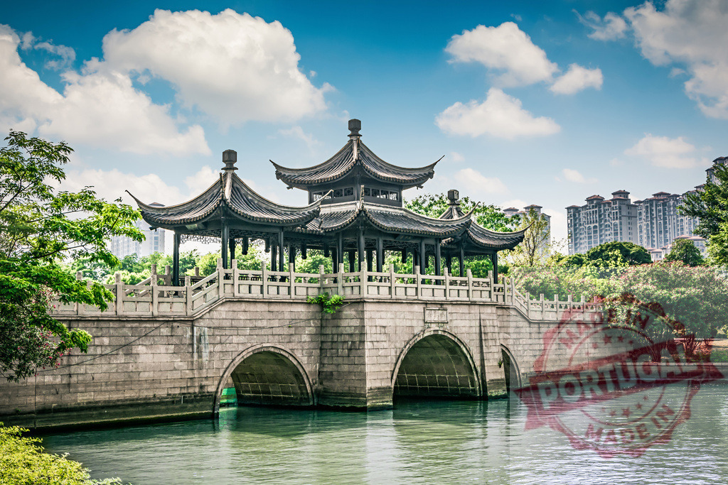 Traditional Chinese bridge architecture spanning river under blue sky | Stone bridge with elaborate pavilion architecture across calm water with trees and city buildings - Realized with Pictrs.com