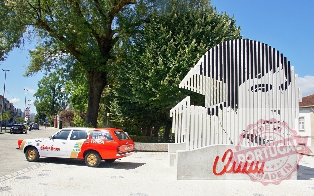 Vintage car parked near modern art installation representing Eusébio da Silva Ferreira in Portugal | Red and white vintage car parked near a modern art installation representing portuguese soccer player Eusébio, in a sunny day - Realized with Pictrs.com