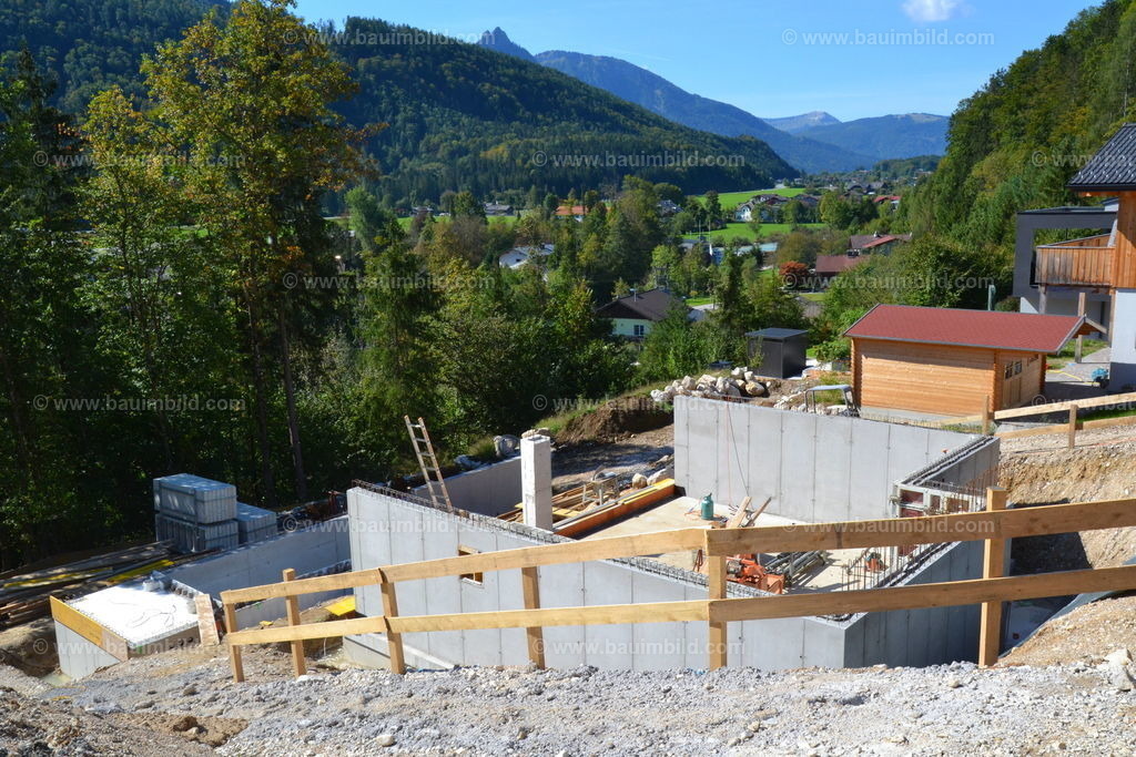 Betonaußenwände | Untergeschoß / Keller in Hanglage mit Außenwänden aus Beton, Baugrube mit Absturzsicherung, dahinter Berglandschaft mit blauem Himmel