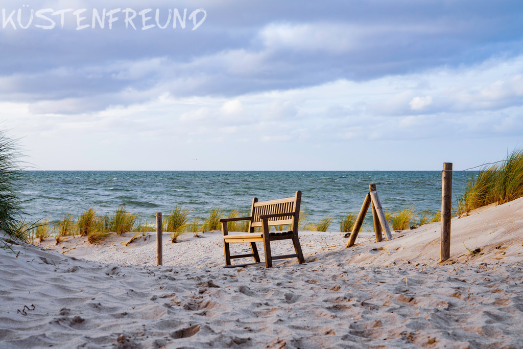 Bank der Stille in sanften Dünen – Ostsee Bilder | Dieses Wandbild zeigt eine Bank der „Stille“ am Dünenweg der zum Strand führt, umgeben von sanften Dünen. Der vordere Bildbereich sowie der Hintergrund mit Ostsee und Himmel sind in einem dezenten Bokeh-Effekt gehalten. Diese bewusste Unschärfe unterstreicht den Moment der Ruhe und Gelassenheit, den diese Szene vermittelt. Ein besonderes Ostsee Bild, das die Essenz von "NO MIND" einfängt – nur du und die Küste. Genieße deinen ganz persönlichen Moment der Stille.<br><br><strong>Tipp:</strong> Statt das klassische Querformat zu wählen, kannst du dieses Wandbild mit der stillen Bank am Dünenweg auch flexibel zuschneiden – ob als quadratisches Wandbild, Hochkantformat oder Panorama. So wird dein persönliches Ostsee Bild zum perfekten Ort der Ruhe in deinem Zuhause.