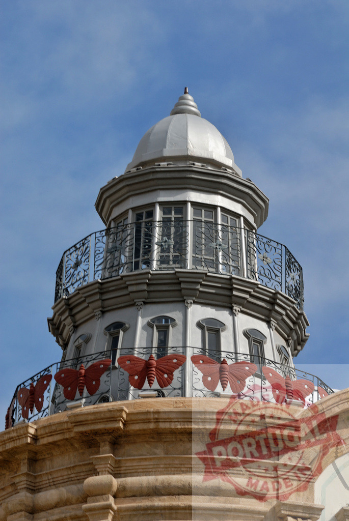Architectural tower dome featuring red butterfly railing details | Ornate architectural tower dome with decorative red butterflies on balconies against a blue sky - Realisiert mit Pictrs.com