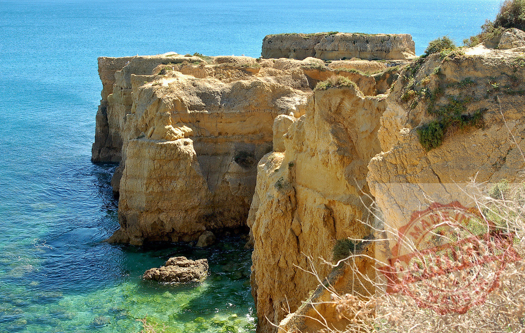 Coastal cliffs embracing clear turquoise ocean water | Rugged coastal cliffs meet the clear turquoise ocean water on a sunny day - Realized with Pictrs.com