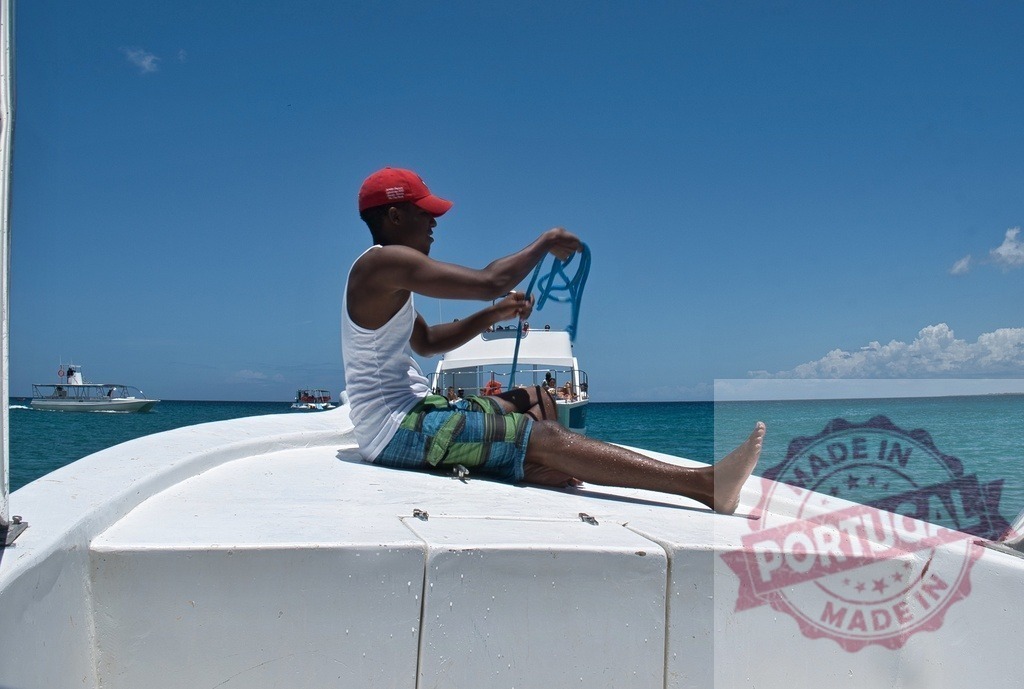 Man holding rope onboard moving boat on ocean | Man holding a rope while sitting on the bow of a moving boat on the ocean - Realized with Pictrs.com
