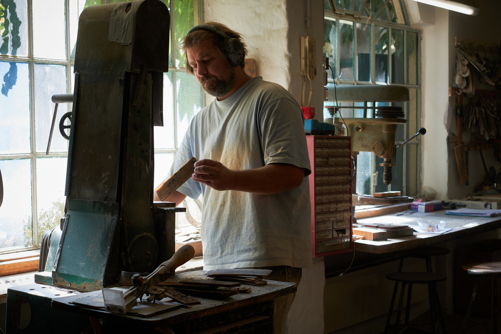 Hornmanufaktur, Herr Petz an der Schleifmaschine | Wien, Austria - August 09, 2022; Hornmanufaktur Thomas Petz; Schleifarbeit in der Werkstatt mit Lärmschutz. - Realisiert mit Pictrs.com