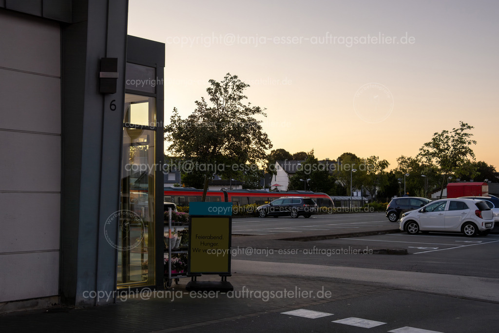 Abendliches Lebensmittelgeschäft an den Briloner Arkaden | Abendliches Lebensmittelgeschäft bei den Briloner Arkaden. Im Hintergrund sind der Bahnhof und ein Zug zu sehen. Auf dem Schild steht deutscher Text: Feierabend, Hunger, wir verstehen. 