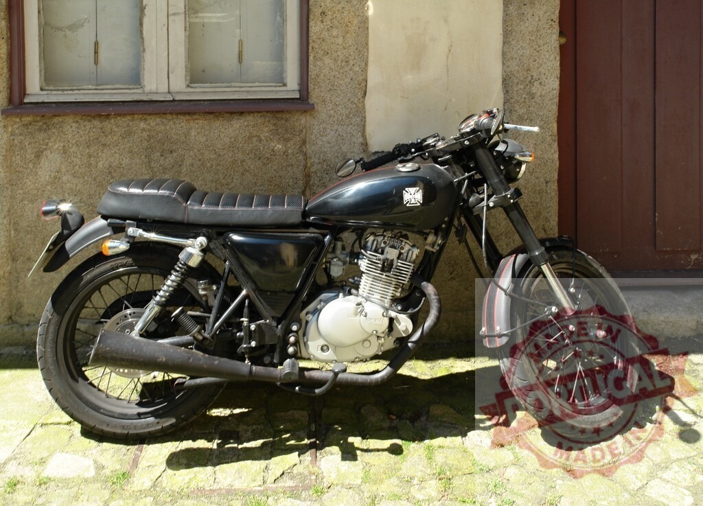 Black Suzuki GN 125 motorcycle parked near a house | Customized black Suzuki GN 125 motorcycle parked near a house with window and brown door - Realisiert mit Pictrs.com