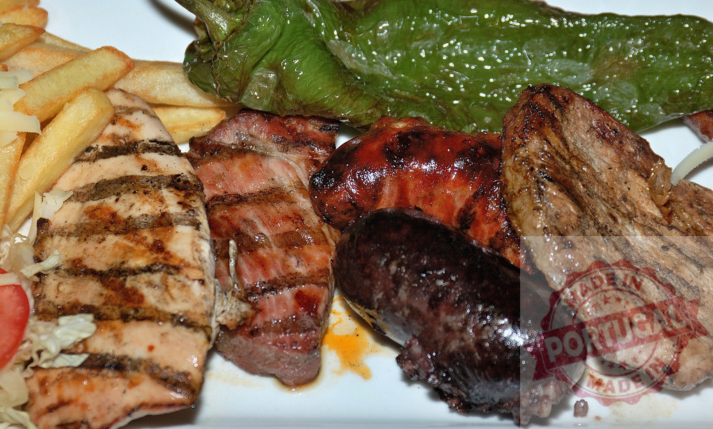 Argentine parrillada plate with mixed grilled meats and fries | Mixed grilled meats, sausage, blood sausage, peppers, and french fries served on a plate - Realized with Pictrs.com