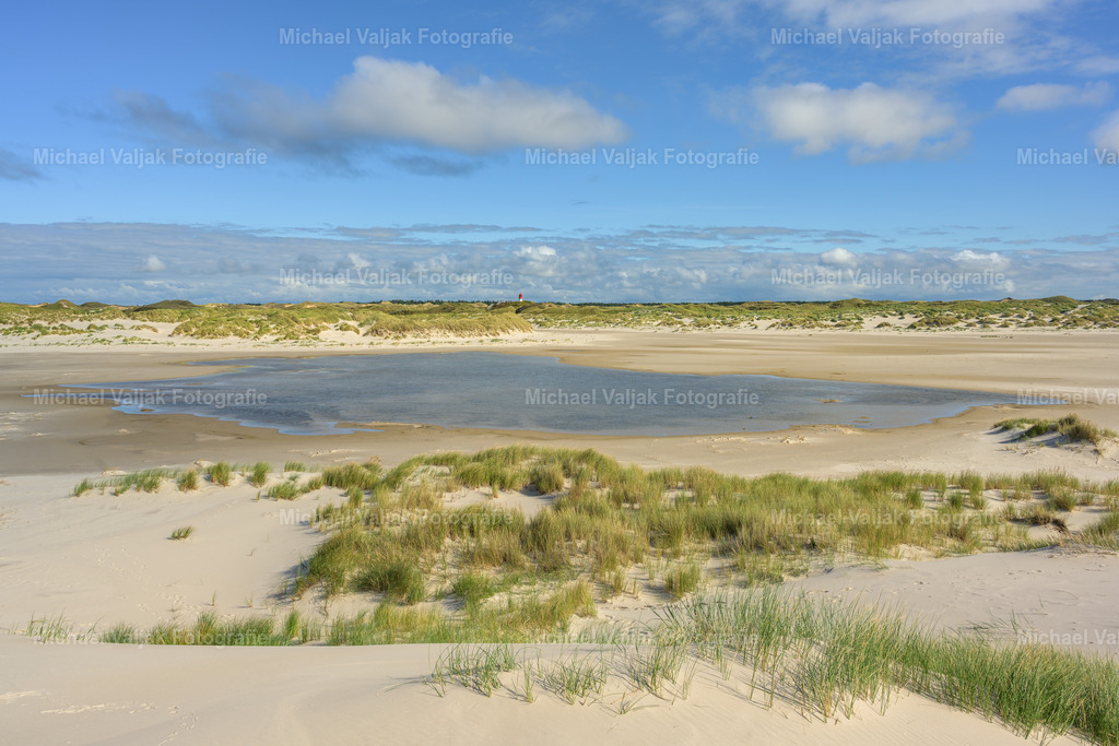Blick vom Kniepsand zu den Amrumer Dünen mit dem Quermarkenfeuer | Der Kniepsand, bekannt als einer der längsten Strände Norddeutschlands, bietet eine atemberaubende Aussicht auf die Amrumer Dünen und das historische Quermarkenfeuer. Dieses Leuchtfeuer, das seit Dezember 1984 ferngesteuert wird, ist ein markantes Wahrzeichen der Insel Amrum. Besucher können von der Aussichtsplattform am Fuß des Leuchtturms den Panoramablick über die Heide und die Dünen bis hin zum Kniepsand genießen. Bei klarer Sicht reicht der Blick sogar bis zur Südspitze von Sylt mit dem Leuchtturm von Hörnum. - Realisiert mit Pictrs.com