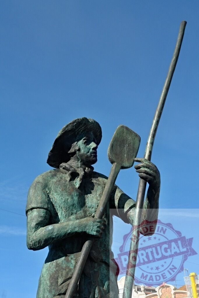 Bronze statue of worker holding shovel and pole against blue sky | Bronze statue of a worker wearing a hat, holding a shovel and a long pole - Realisiert mit Pictrs.com