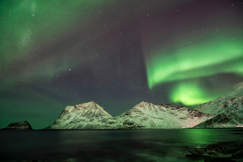 Nordlicht über dem Haukland Strand – Lofoten | Grün leuchtende Polarlichter tanzen über verschneiten Bergen am Haukland Strand. Die klare Nacht, die ruhige See und das Naturwunder Aurora Borealis machen dieses Bild zu einem besonderen Blickfang – ruhig, kraftvoll und faszinierend. - Realisiert mit Pictrs.com