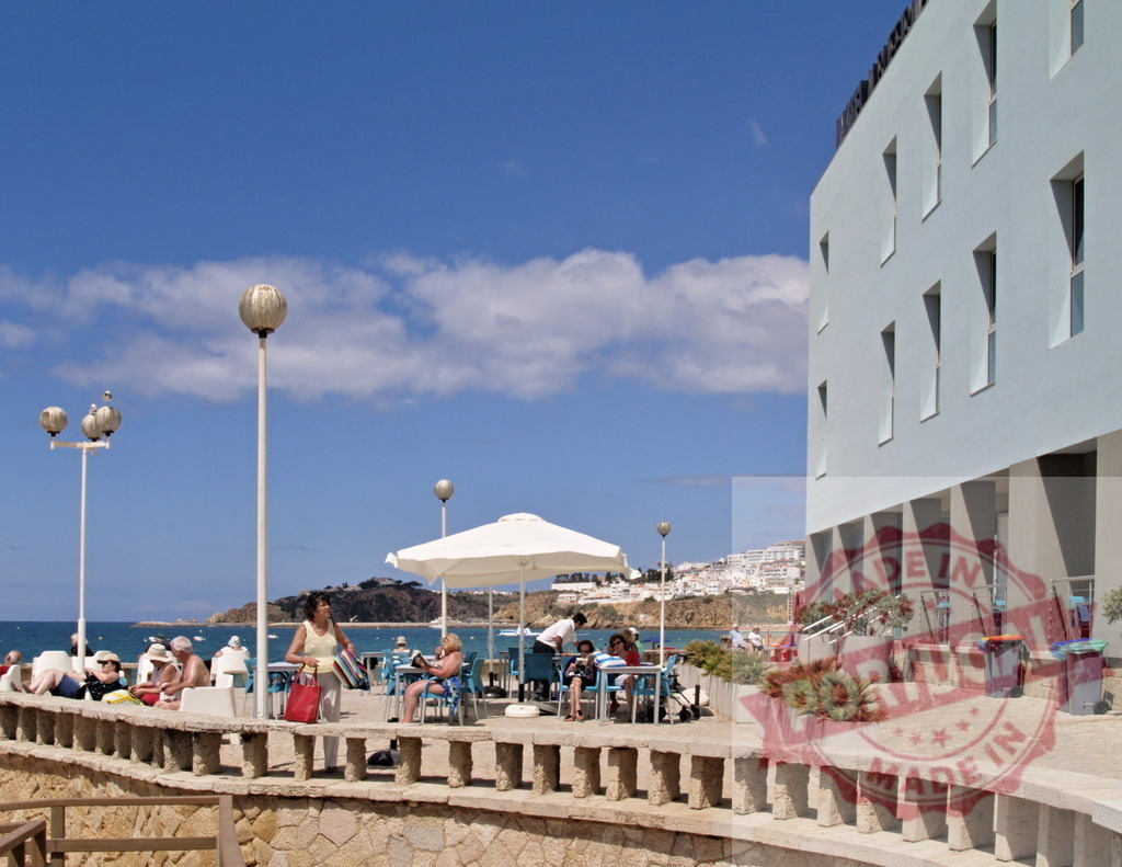People relaxing at a beachside cafe and hotel terrace | People enjoying summer vacation by the ocean, sitting at tables and sunbathing near a modern hotel - Realisiert mit Pictrs.com
