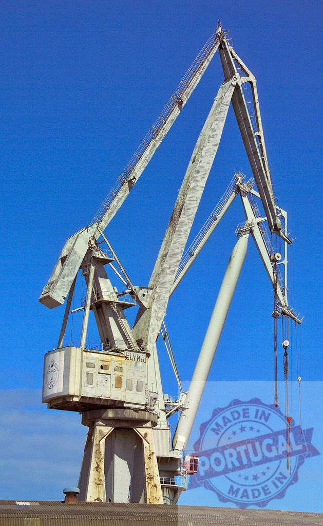 Industrial port crane operating under clear blue sky. Spain - Bilbao | Large industrial harbor crane standing tall against a bright blue sky, ready for work - Realized with Pictrs.com