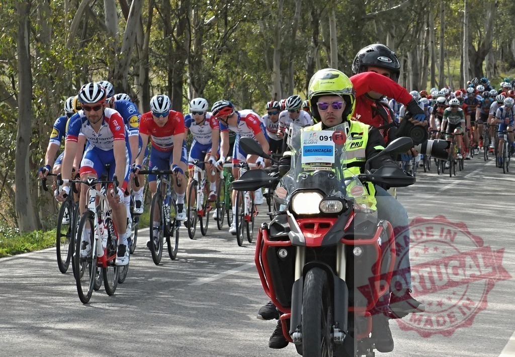 Professional cyclists racing in a peloton with motorcycle escort | Cyclists competing in a professional road cycling race, escorted by a motorcycle with a camera operator - Realisiert mit Pictrs.com