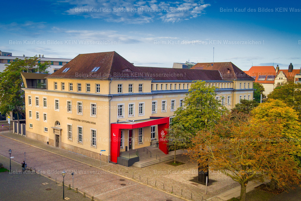 Magdeburg Sehenswürdigkeiten Dommusuem Ottonianum-0002 | Diese stimmungsvolle Luftaufnahme zeigt das Dommuseum Ottonianum im Herzen der Magdeburger Altstadt aus einer tiefen Drohnenperspektive. Eingebettet in die herbstlich gefärbten Baumkronen entfaltet das moderne Museumsgebäude seine besondere architektonische Wirkung. Die leuchtenden Gelb-, Orange- und Rottöne der Bäume bilden einen harmonischen Kontrast zur klaren Formensprache des Gebäudes und unterstreichen die gelungene Verbindung von zeitgenössischer Architektur und historischer Umgebung am Magdeburger Dom.Dieses Motiv zeigt beispielhaft die Vielfalt der Architektur-Highlights, aus denen Ihr individueller Luftbildkalender zusammengestellt werden kann. Moderne Museumsbauten, historische Wahrzeichen, denkmalgeschützte Gebäude oder markante Unternehmensarchitektur – Sie entscheiden selbst, welche Bauwerke Ihren Kalender prägen sollen. Alle gezeigten Luftaufnahmen dienen als Inspiration und können jederzeit durch andere Motive aus dem umfangreichen Luftbildarchiv ersetzt oder ergänzt werden.So entsteht ein hochwertiger Firmenkalender mit persönlichem und regionalem Bezug. Sie wählen Ihre Wunschmotive aus, ich übernehme die professionelle Gestaltung und Umsetzung. Die individuelle Motivauswahl gehört selbstverständlich zum Service und ermöglicht einen Kalender, der die architektonische Vielfalt Magdeburgs genau nach Ihren Vorstellungen präsentiert. - Realisiert mit Pictrs.com
