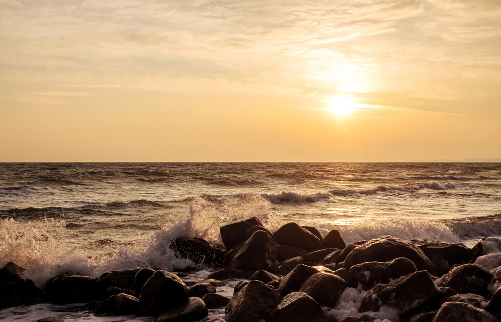 Wandbild: Brandung der stürmischen Ostsee im Morenrot | Dieses Wandbild im Querformat zeigt einen schönen Sonnenaufgang an der Ostsee. Im Vordergrund brechen die Wellen an der Steinmole. Der Himmel leuchtet in schönen warmen Farben. - Realisiert mit Pictrs.com