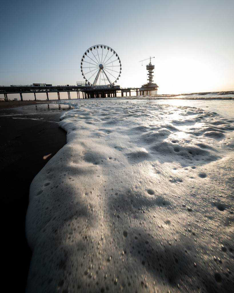 Wasserlauf zum Riesenrad von Scheveningen | Eine Wasserspur im Sand führt den Blick direkt zum Riesenrad auf dem Pier von Scheveningen während des Sonnenuntergangs. - Realisiert mit Pictrs.com