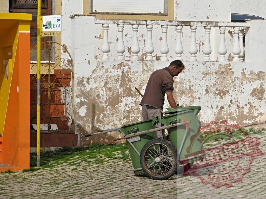 City worker collecting garbage with handcart on cobblestone street | City worker collecting garbage using a handcart on a cobblestone street by an old wall - Realisiert mit Pictrs.com