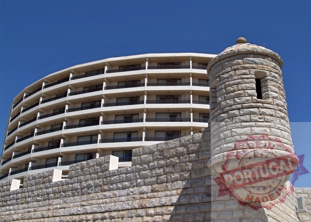 Modern building and ancient stone fort contrasting architecture | Modern building rising above a traditional stone wall with a watchtower under a clear blue sky - Realisiert mit Pictrs.com