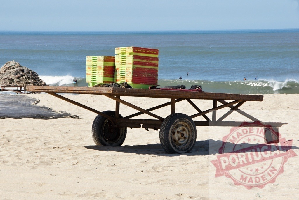 Empty merchant cart with crates on beach | Metal transport cart with colorful crates resting on a sandy beach by the ocean - Realisiert mit Pictrs.com