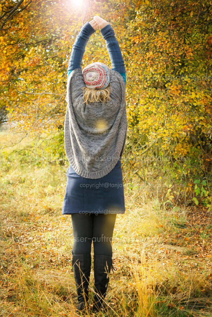 Woman stretches the back in autumn scenery | Frau mit Strickkleidung in sonniger Herbstlandschaft. Sie trägt einen Poncho und einen Rock mit Stiefeln. Wollmütze. Sie streckt ihren Rücken. Rückseite. 