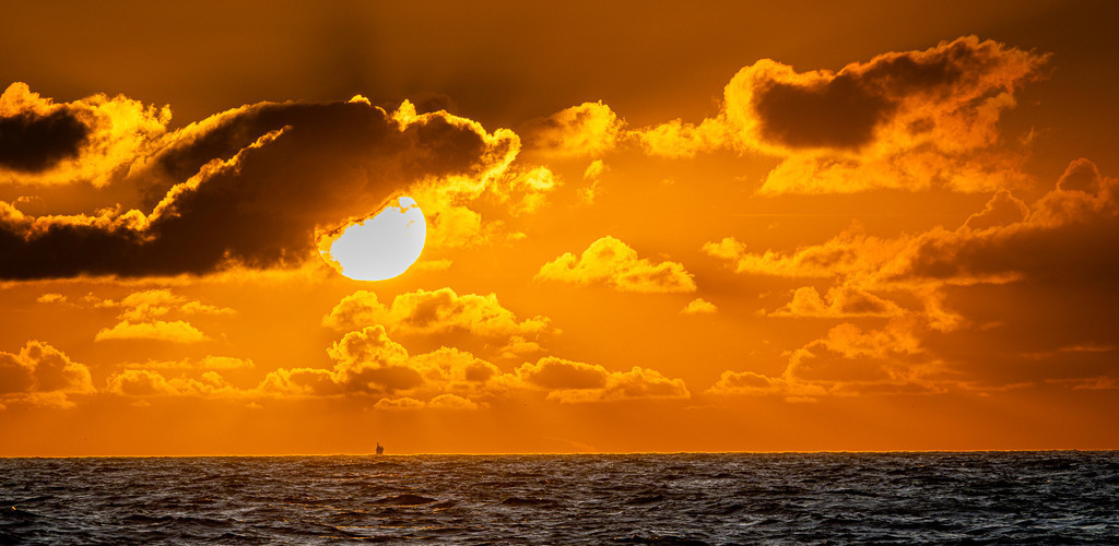 Goldene Abendstimmung am Horizont | Strahlende Abendsonne bricht durch eine dichte Wolkenschicht über der Nordsee vor der Küste der niederländischen Insel Texel. Das grelle Licht taucht den Himmel in ein intensives Orange-Gold, während sich die untergehende Sonne auf der dunklen Wasseroberfläche spiegelt. Redaktionell vielseitig einsetzbar für Naturaufnahmen, Reiseberichte, Stimmungsbilder und Illustrationen zum Thema Küstenlandschaft, Urlaub und Abendstimmung. - Realisiert mit Pictrs.com