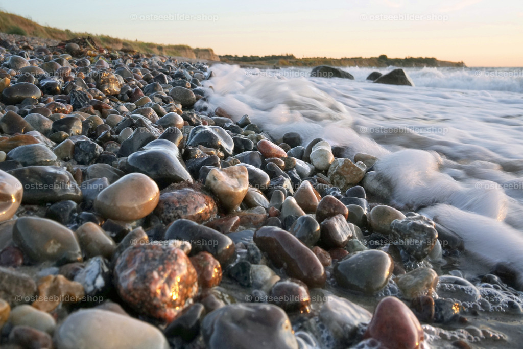 Die letzten Zentimeter einer auslaufenden Welle | Auslaufende Schaumkronen treffen auf einen Strand voller farbiger Ostseesteine.