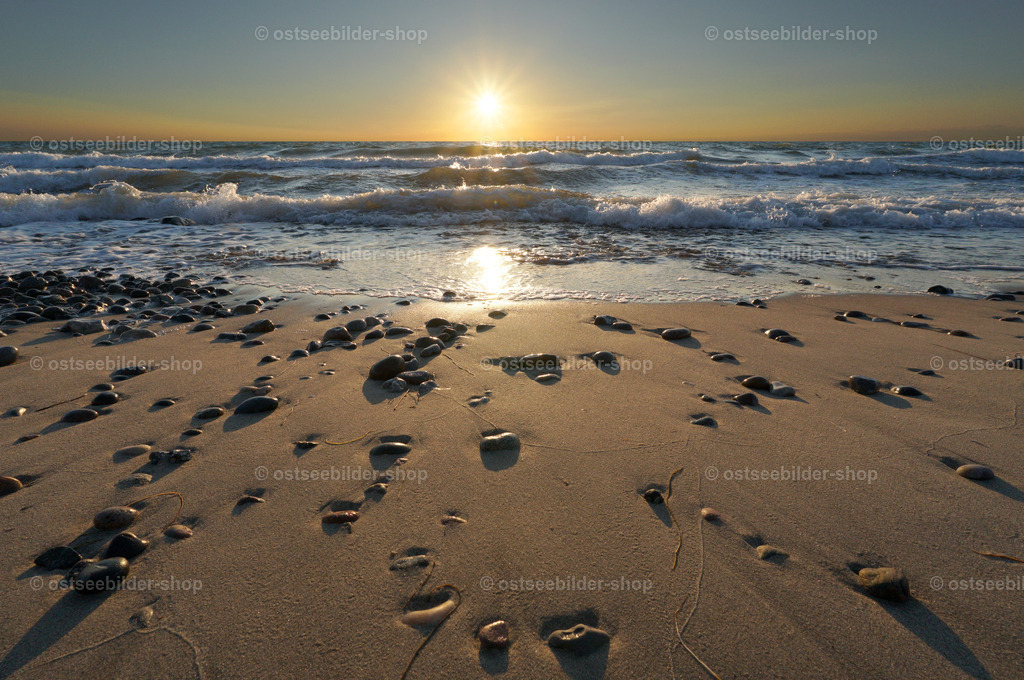 Steine zwischen Strand und Meer | Der Tag geht zu Ende und die Wellen werden kürzer. Im glatten Strandsaum ragen Steine halb aus dem Sand heraus. 