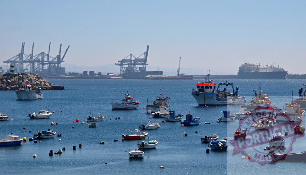 Fishing boats in harbor with industrial port cranes | Fishing boats anchored in a harbor bay with large shipping port and tanker in background - Realized with Pictrs.com