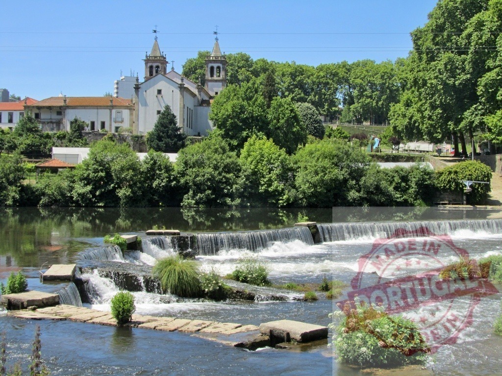 Ave River cascading weir with Santo Tirso church. Portugal - Norte | Ave River flowing over a weir with Santo Tirso church and green trees on the bank - Realized with Pictrs.com