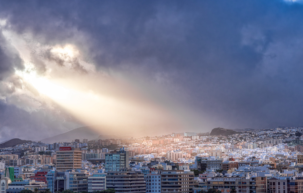 Dramatisches Lichtspektakel über Santa Cruz de Tenerife,Teneriffa | Auf diesem Bild ist die Stadt Santa Cruz de Tenerife, die Hauptstadt der gleichnamigen Insel Teneriffa, zu sehen. Es handelt sich um die zweitgrößte Stadt des kanarischen Archipels mit über 200.000 Einwohnern. Die Stadt wurde 1496 gegründet und liegt im Nordosten der Insel. Das Bild zeigt eine dramatische Wolkenstimmung, bei der Sonnenstrahlen durch eine Wolkendecke auf die dichte Bebauung der Stadt fallen. - Realisiert mit Pictrs.com