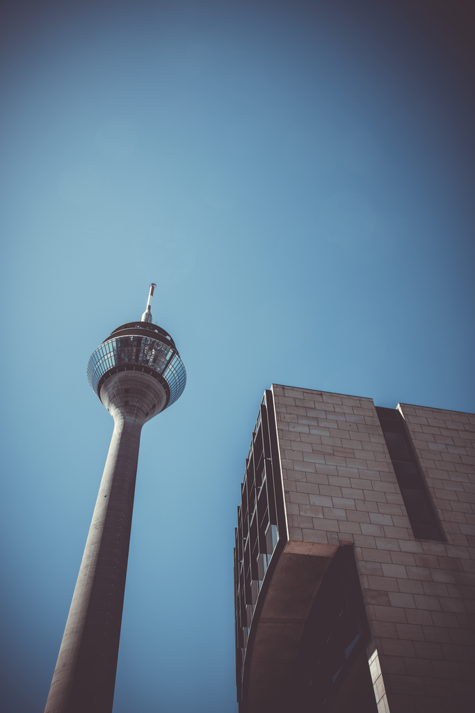 Skyward | Düsseldorf | Der Düsseldorfer Rheinturm erhebt sich aus einer ungewöhnlichen Perspektive in den klaren blauen Himmel. Die starke Untersicht und die reduzierte Komposition betonen Höhe, Linienführung und die geometrische Wirkung der urbanen Architektur.Ein minimalistisches Architekturfoto, das eines der bekanntesten Wahrzeichen Düsseldorfs bewusst aus einer weniger klassischen Perspektive zeigt. - Realisiert mit Pictrs.com